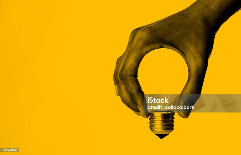 Light Bulb in Hand Light bulb in human hand, yellow background. Innovation Stock Photo