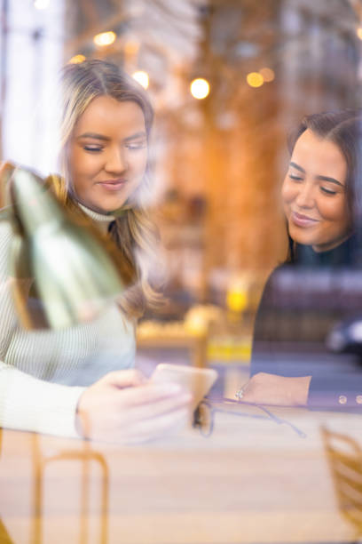 istock Two Female Friends Looking At Smartphone In Cafe seen through window 1155742771