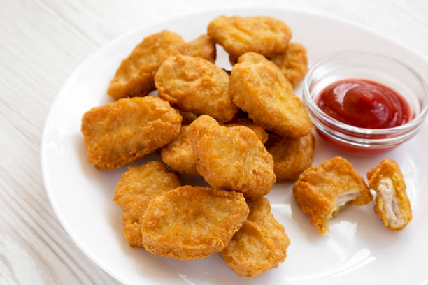 istock Chicken nuggets with ketchup on a white plate on a white wooden background, low angle view. Close-up. 1155749417