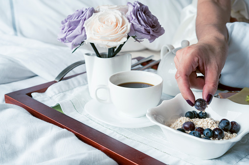 latina woman enjoys delicious breakfast in her bed composed of cup of coffee cereal with grapes and beautiful flowers decorating