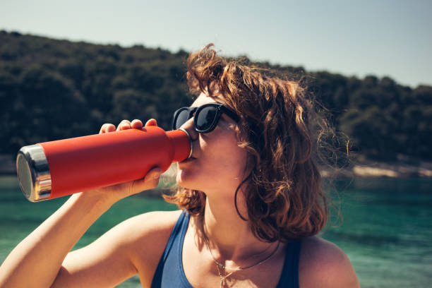 Young woman drinking water from an insulated bottle in nature stock photo