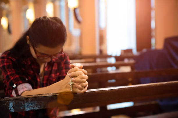 młoda kobieta siedzi na ławce w kościele i modli się do boga. ręce złożone w koncepcji modlitewnej dla wiary. - forgiveness praying men silhouette zdjęcia i obrazy z banku zdjęć