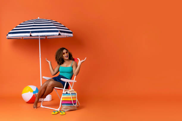sorprendido mujer afroamericana sentada en una silla de playa - summer people furniture vacations fotografías e imágenes de stock