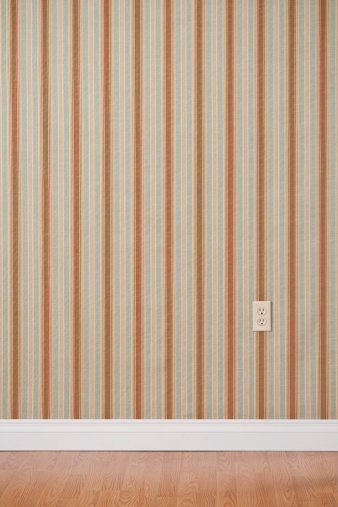 Empty domestic room with wall outlet. The wall has a white baseboard and striped wallpaper.*