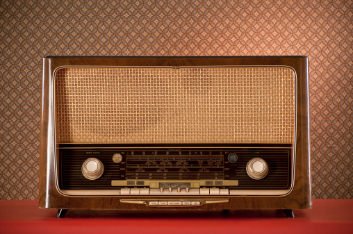 Old radio sitting on red desk. The wall has a geometric pattern wallpaper.*