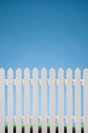White picket fence against blue sky with grass in the bottom. Shot in the studio.