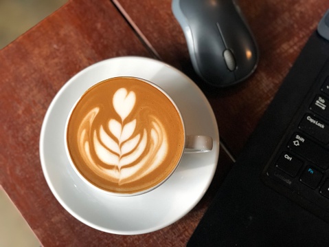 Latte on wooden table with laptop and mouse