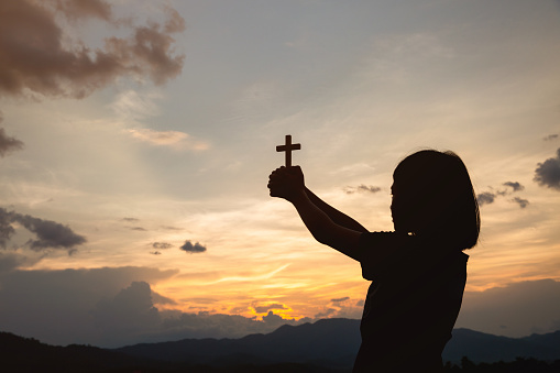 Hand of a girl holding a cross at sunrise, Eucharist Therapy Bless God Helping Repent Catholic Easter Lent Mind Pray. Prayer to God Christian Religion concept background.