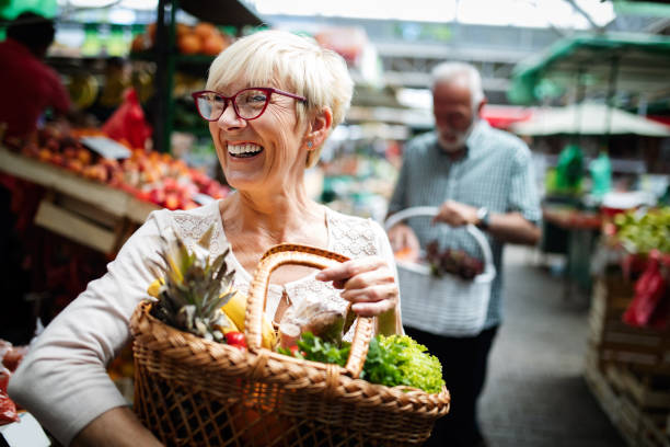 la pareja mayor que compra verduras y frutas frescas en el mercado local - mercado fotografías e imágenes de stock