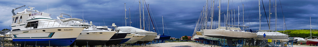 Sukosani, Croatia – October 07, 2017: Panorama view of Dark clouds over dry storage of yachts and sailing boats at Marina Sukosani near Zadar on Adriatic coast in Croatia. It is one of the biggest marina on Croatian Adriatic coast. There is a man walking on Pier to sailing boat.