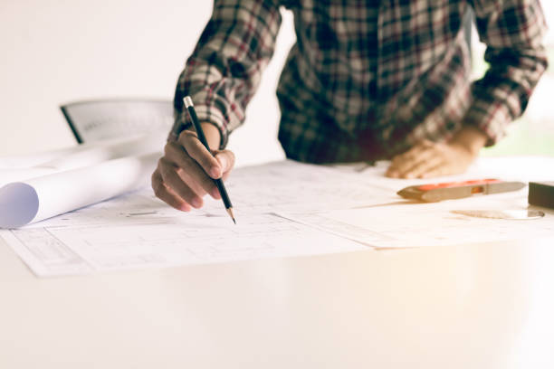 istock Hand of young engineering man drawing on blueprint at table in office room. 1155835045
