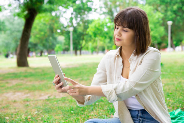 istock Serious pretty woman using tablet and sitting on lawn 1155839681