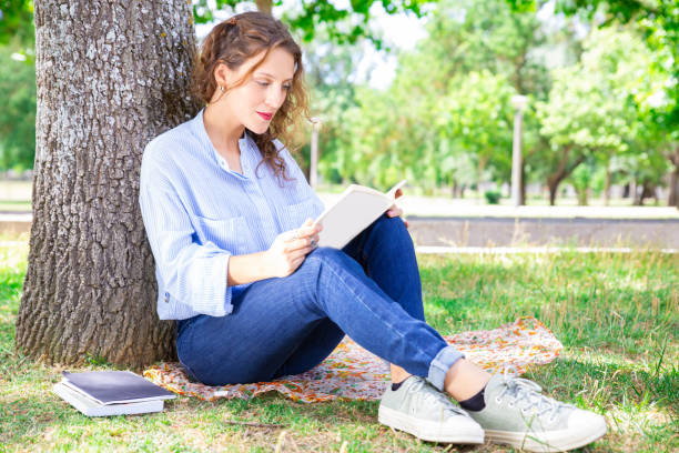 istock Concentrated young woman with wavy hair reading interesting book 1155840473