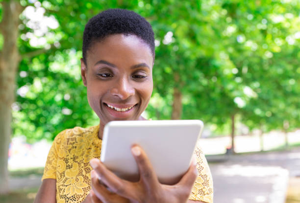 istock Jolly black woman laughing while using tablet outdoors 1155840514