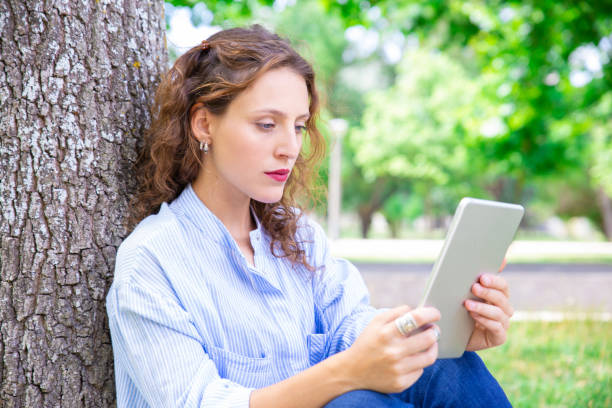 istock Serious young woman reading article on gadget outdoors 1155840545