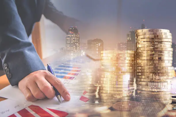 Double exposure of businessman working with laptop at office and stack of coin and city night background