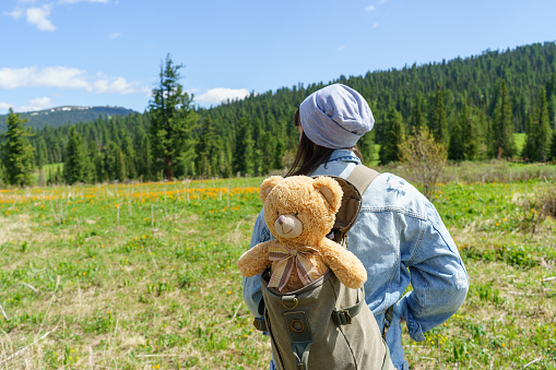 Woman in blue denim jacket holding teddy bear in beautiful Sayan mountains