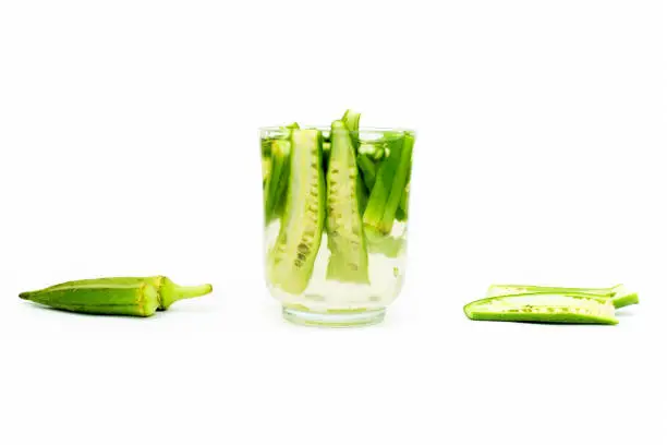 Photo of Popular Okra drink isolated on white with some okra pods in water and some of them on the surface and isolated on white.