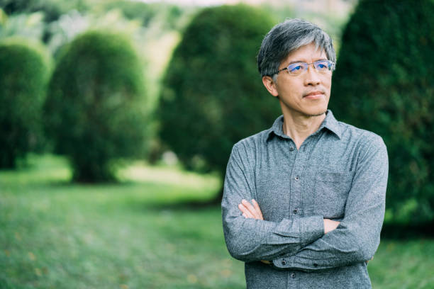 istock Asian man standing arms crossed in park alone 1155846683