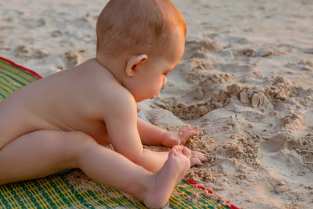 Baby playing and eat sand on the tropical beach. Infant girl of nine month.  Sunset light. Golden hour. stock photo