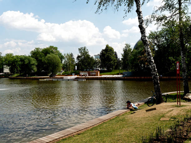 Moscow, Russia - May 28, 2019: a girl is reading under the birch tree near the pond in VDNKh