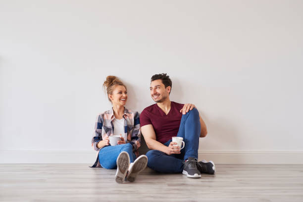 コーヒーを飲みながら笑顔のカップルが家に引っ越しから休憩 - floor sitting ストックフォトと画像