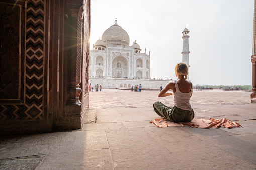 Young woman practicing yoga in India at the famous Taj Mahal at sunrise - Headstand position upside down- People travel spirituality zen like concept