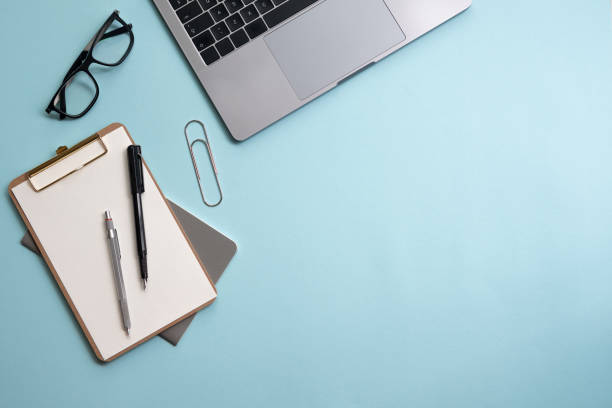 istock Minimal work space - Creative flat lay photo of workspace desk. Top view office desk with laptop, notebooks and glasses on blue color background. 1155867554