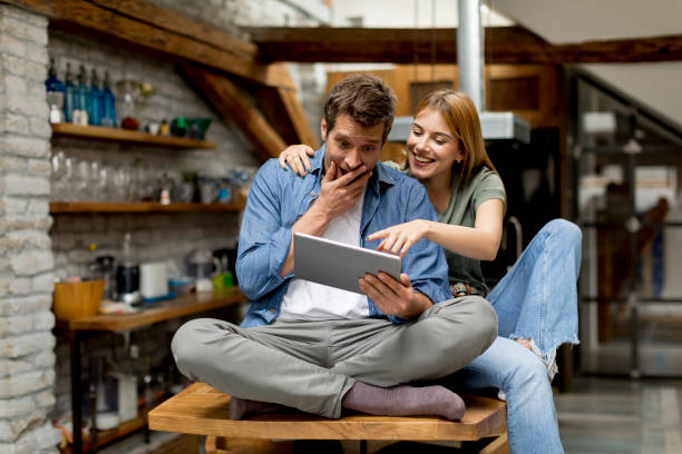 istock Young couple is using a digital tablet and smiling in kitchen at home 1155867608