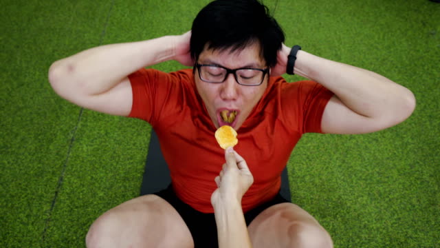 Trainer using chips for incentive or encourage large build Asian man to do sit-ups in gym