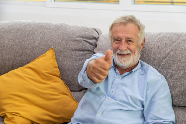 istock Relax happy senior old man eldery sitting on comfortable sofa in living room thumb up looking camera 1155876353