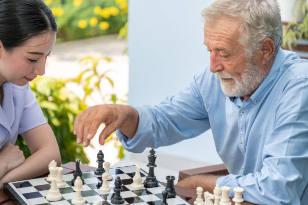 ancianos jugando ajedrez con el cuidador de la enfermera en el hogar de ancianos para el ocio - juego de ajedrez fotografías e imágenes de stock