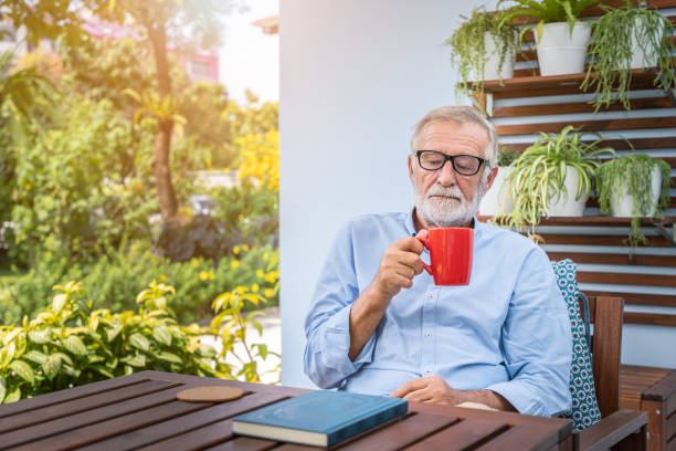 istock Senior elderly man drinking mug of coffee with book on table in garden 1155876383