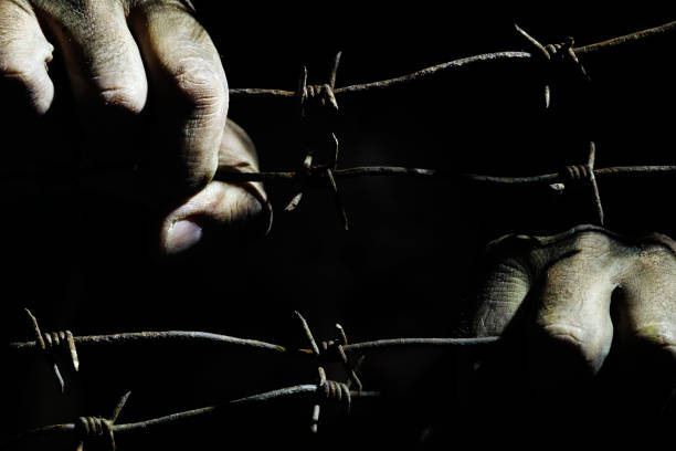 istock Dirty male hands hold stretched rusty barbed wire in the dark 1155876659