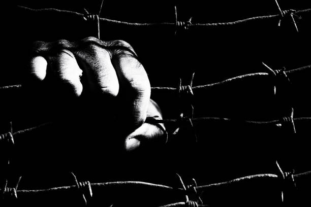 istock Male hand grips stretched rusty barbed wire in the dark 1155876700