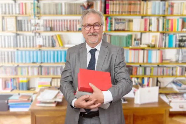 Senior teacher standing holding a book in front of a bookcase