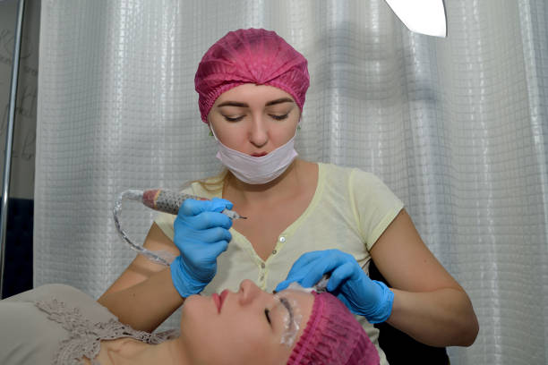 istock Eyebrow microblading procedure. The cosmetologist bent over the patient with a cosmetic tool. Close up. Horizontal view 1155881826