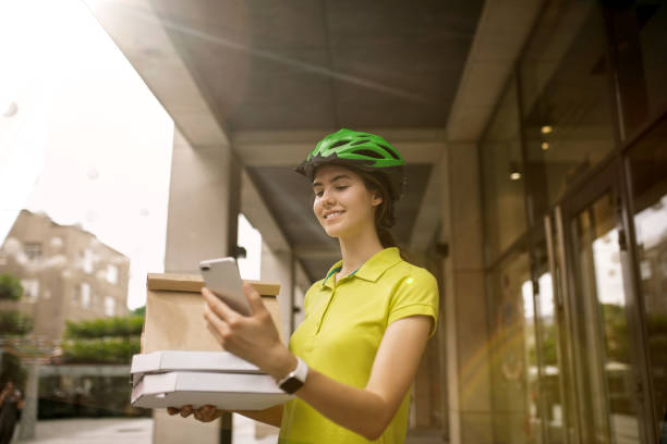 istock Young woman as a courier delivering pizza using gadgets 1155884000