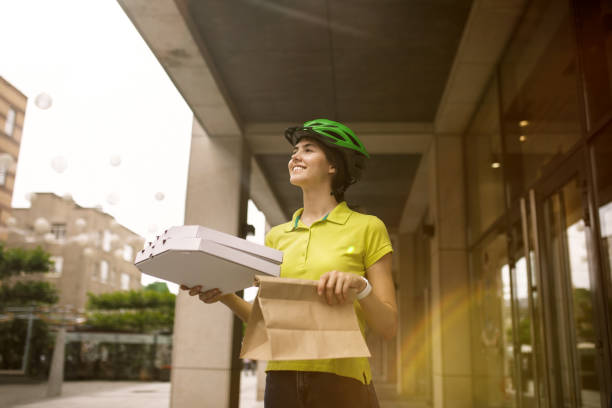 istock Young woman as a courier delivering pizza using gadgets 1155884011
