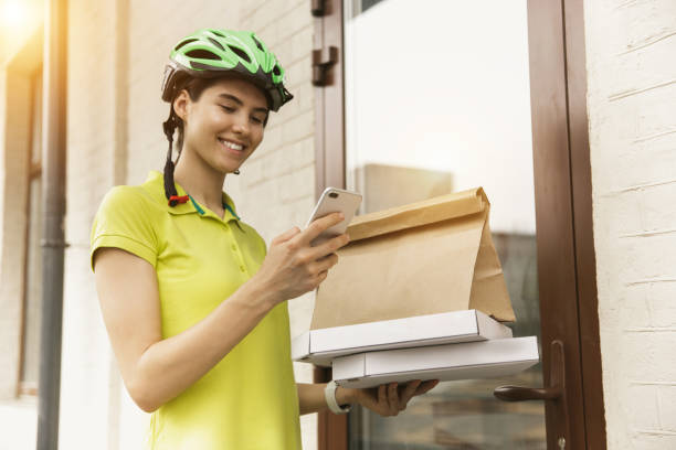 istock Young woman as a courier delivering pizza using gadgets 1155884021
