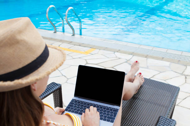istock Young woman using laptop near a swimming pool 1155887513