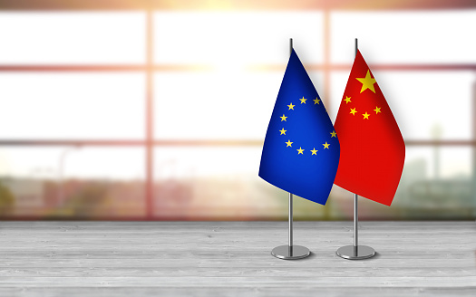 3D chinese and european union flags with metallic pole, standing together on a white wooden desk in front of sunny window background. With large copy space you can write your own titles effectively. Also you can use this compositon as square in social media channels like instagram etc.