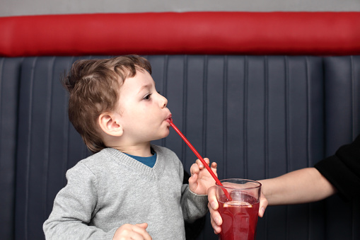 Mother giving fruit drink to her son in the cafe