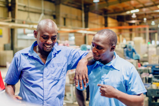 African Factory Supervisor Casually Chatting During their Break Factory, Manual Worker, Quality Control - Factory Supervisors Standing Casually and talking during their break central africa stock pictures, royalty-free photos & images