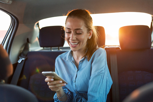 Young woman with smartphone on the back seat of a car