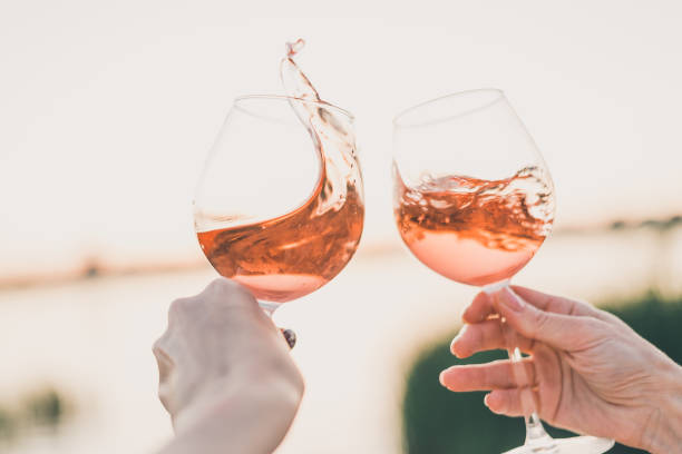 two glasses of rose wine in hands against the sunset sky. - pink champagne fotos imagens e fotografias de stock