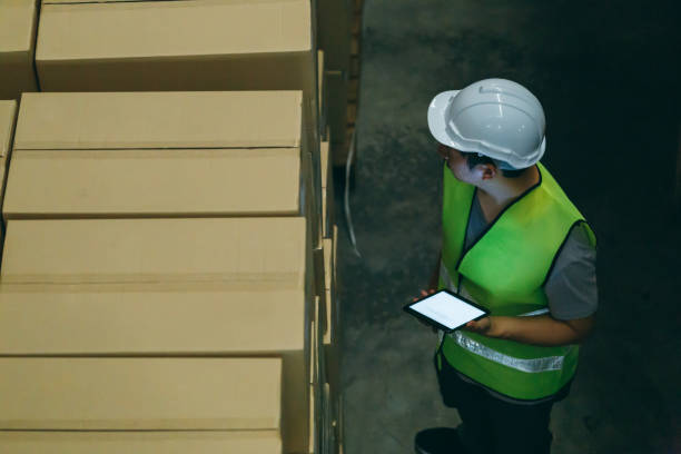 istock Warehouse worker man with safety hard hat is checking order details with a digital tablet at inventory room 1155906798