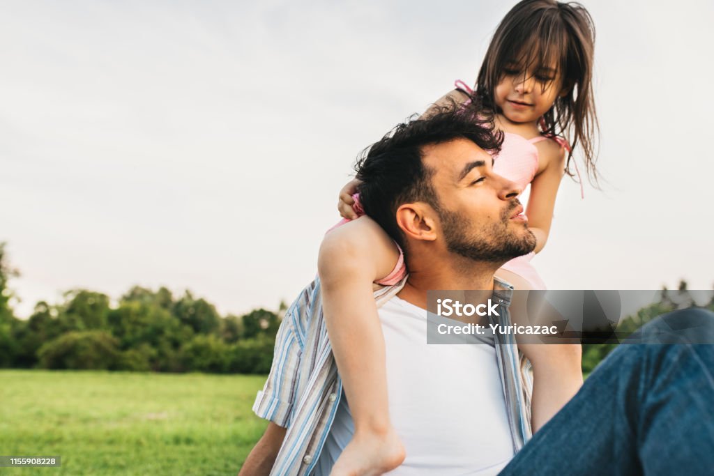 Image of happy cute little girl playing with father in the park during the sunset. Handsome dad is spending time with his little cheerful daughter outdoors. Fathers Day. Daddy and daughter shares love Adult Stock Photo