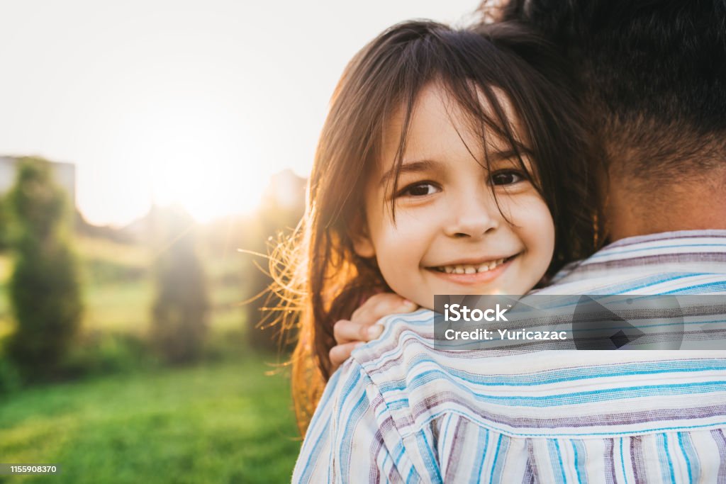 Closeup image of happy daughter embraces her dad feels joyful. Happy cute little girl playing with father in the park, smiling and looking to the camera. Father's Day. Daddy and daughter shares love. Adult Stock Photo