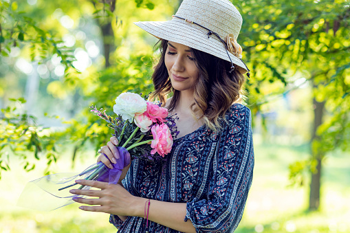Portrait of Attractive Long Haired Young Woman in Dress and Hat Holding a Flowers in the Public Park